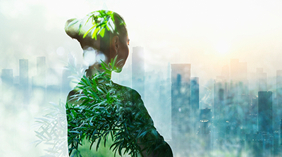 Double exposure image of a person in profile blended with green foliage, set against a hazy city skyline in soft light.